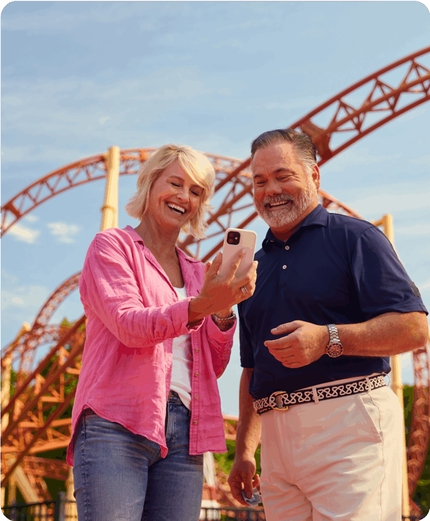Man and woman smiling looking at a phone at a theme park.