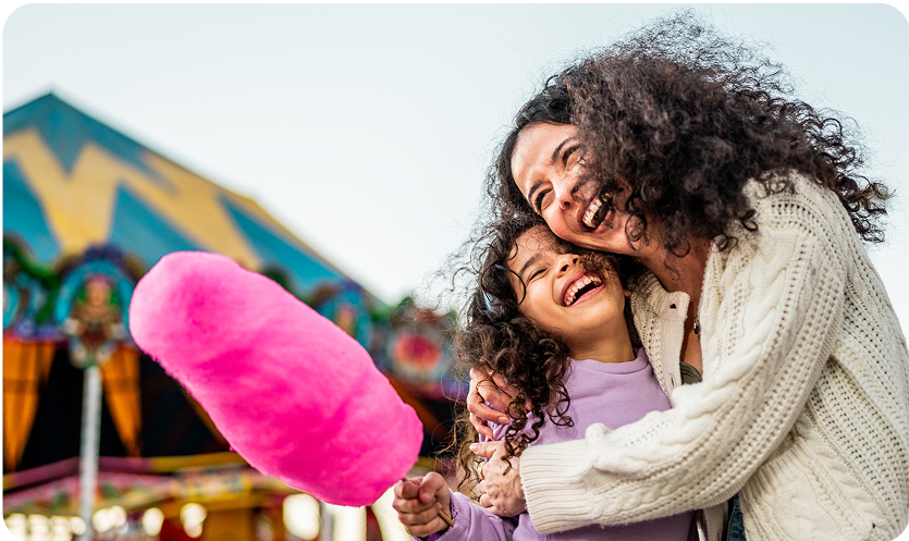 Woman and child at a fair smiling eating cotton candy.