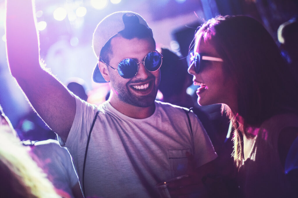 Closeup of two young adults enjoying in a big crowd at a concert party. There are many blurry people in background.