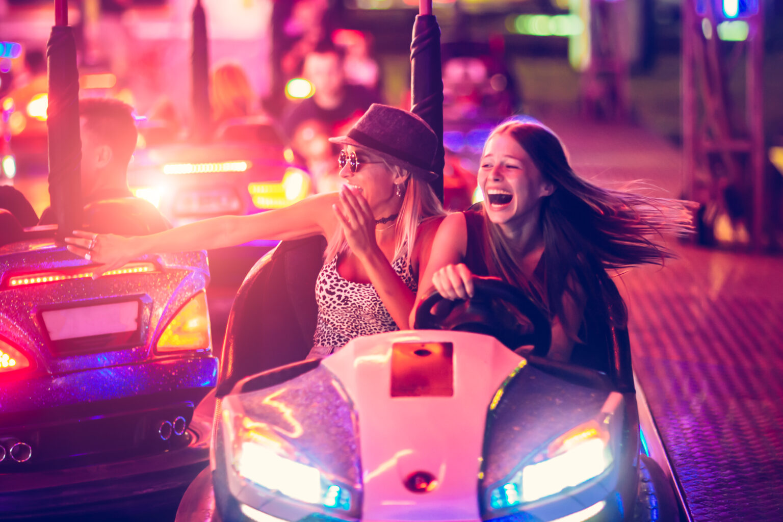Girls having fun in electric bumper car in amusement park
