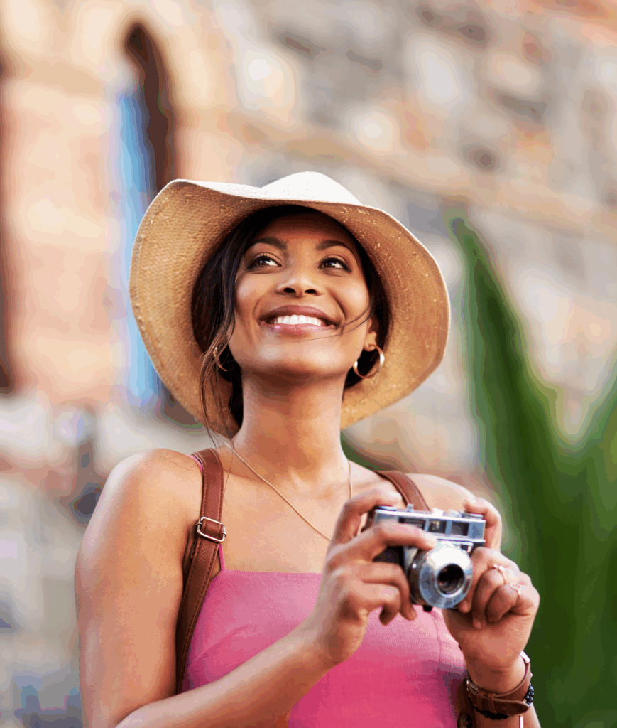 Woman at a tourist site wearing a hat and holidng a camera.