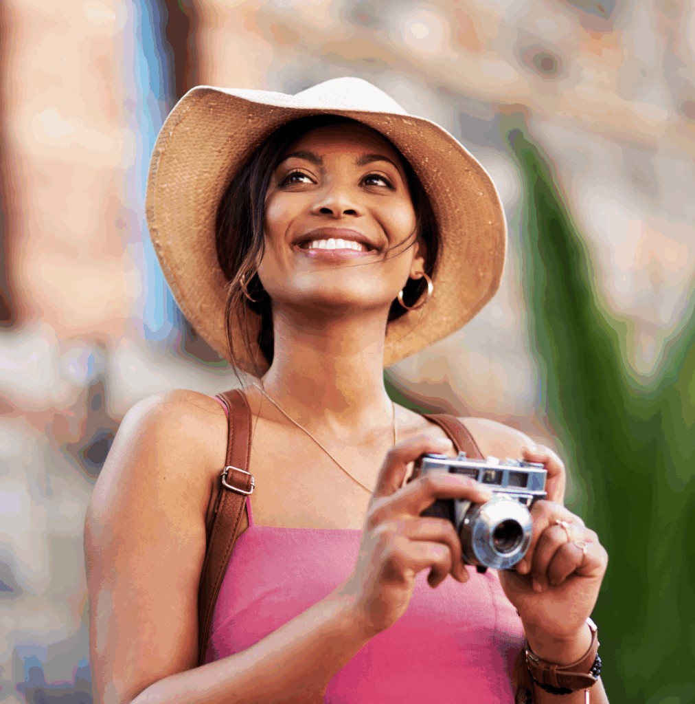 Woman at a tourist site wearing a hat and holidng a camera.