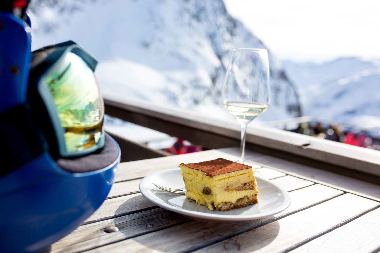 Reflections of snowy mountain in helmet and a glass of wine and plate with tiramisu on table