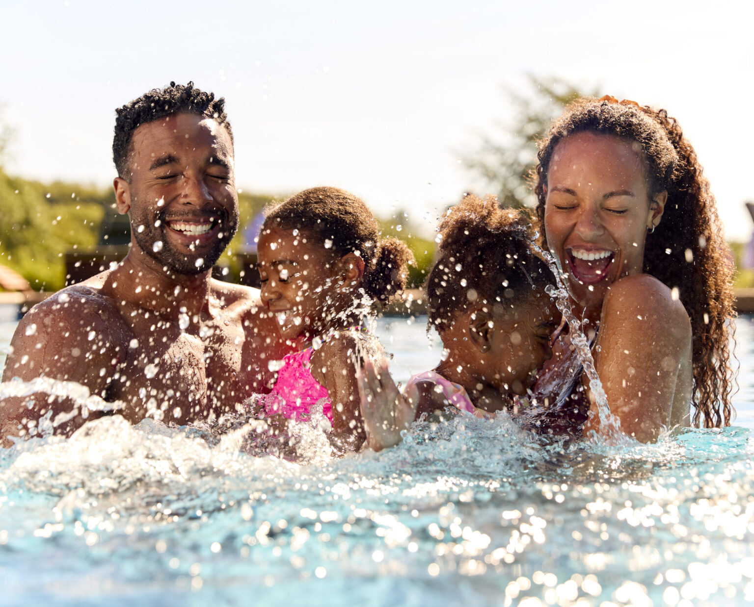 Family On Summer Holiday With Two Girls Being Held In Swimming Pool By Parents And Splashing