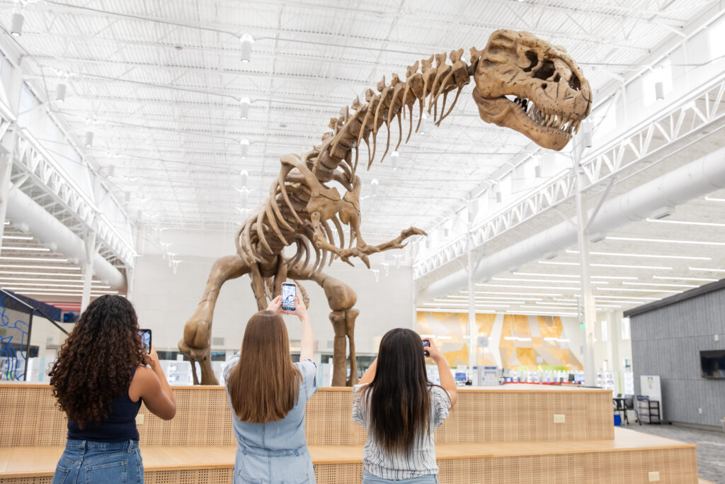 Three female tourists snap photos of a dinosaur fossil in the library lobby.