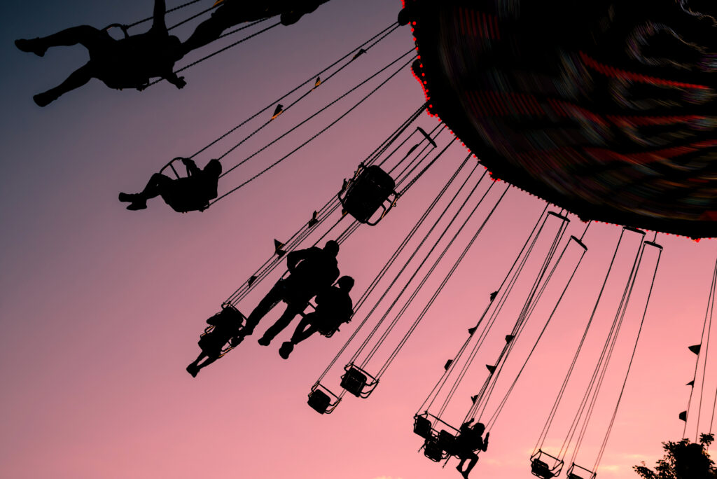 silhouettes of people on swing carousel against purple evening summer sky