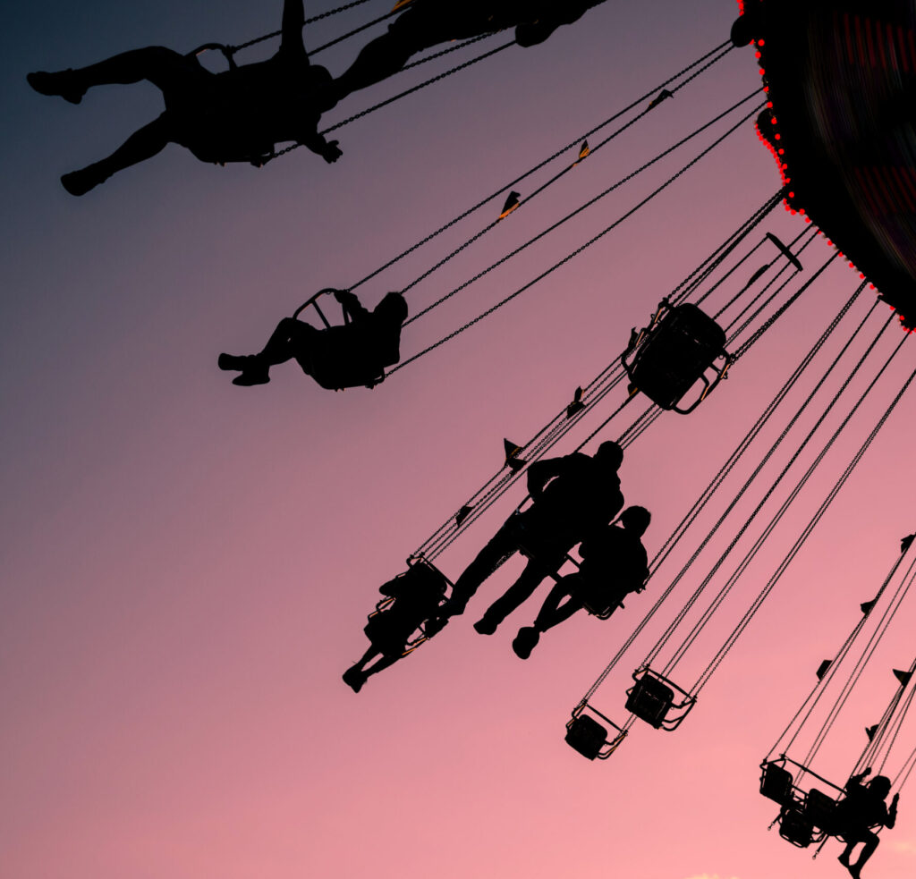 silhouettes of people on swing carousel against purple evening summer sky