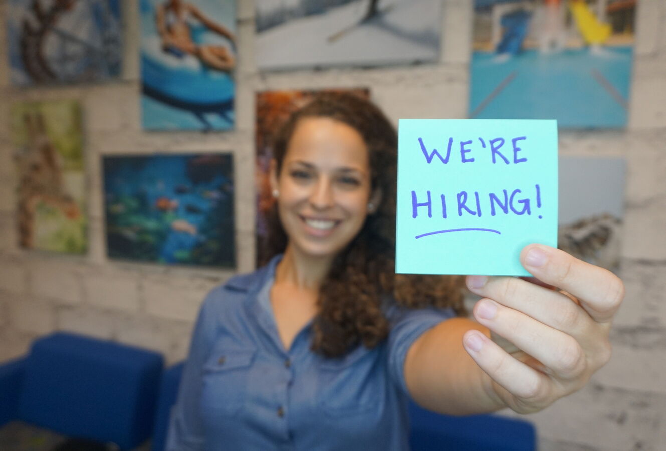 Woman holding a post it that says "We're Hiring"