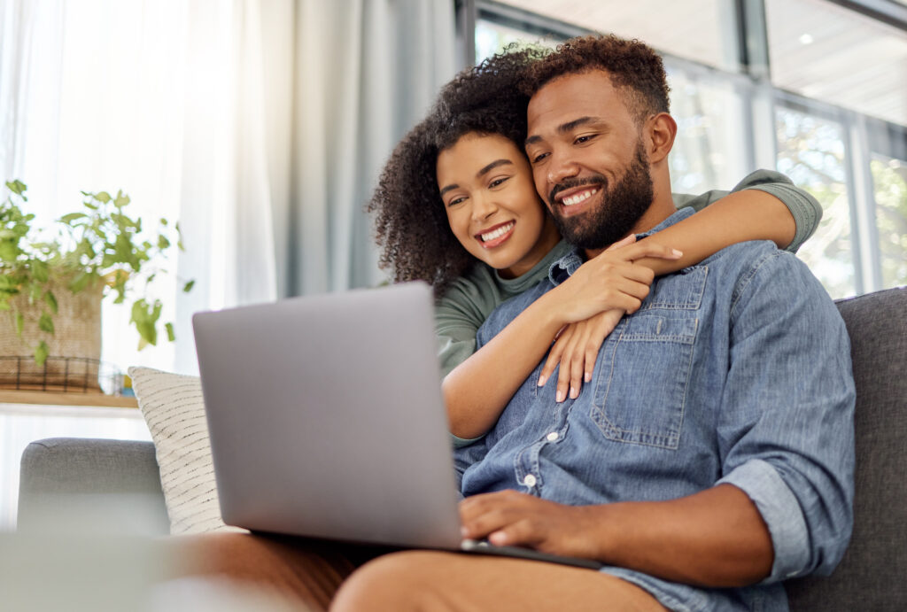 Young happy mixed race couple smiling while using a laptop together at home.