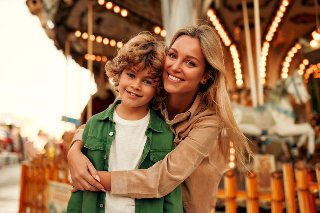A boy blonde child with a curly hairstyle together with his mother came to the amusement park to have fun and ride on the carousels and swings