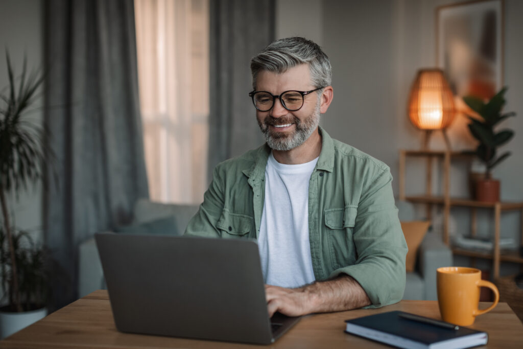 Cheerful elderly european man with beard in glasses on computer