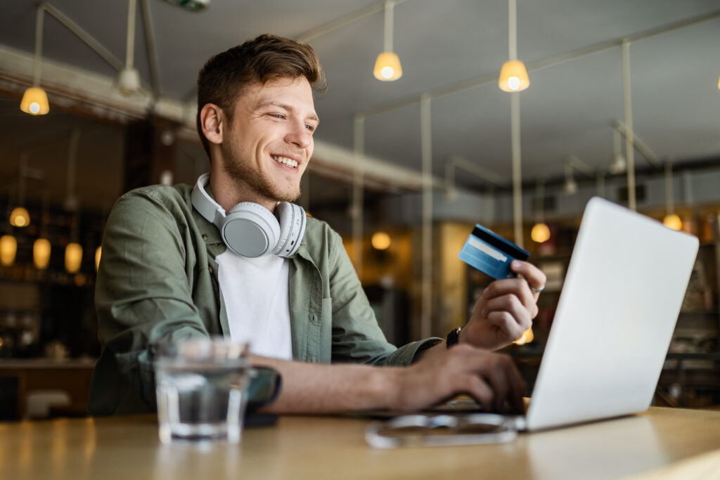 Freelancer man smiling doing remote work at the cafe paying with credit card online