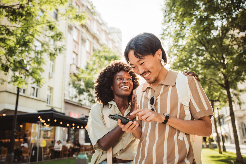 Young tourist couple, walking through the city and checking map on smart phone. Wearing casual clothes. Enjoying in beautiful sunny day